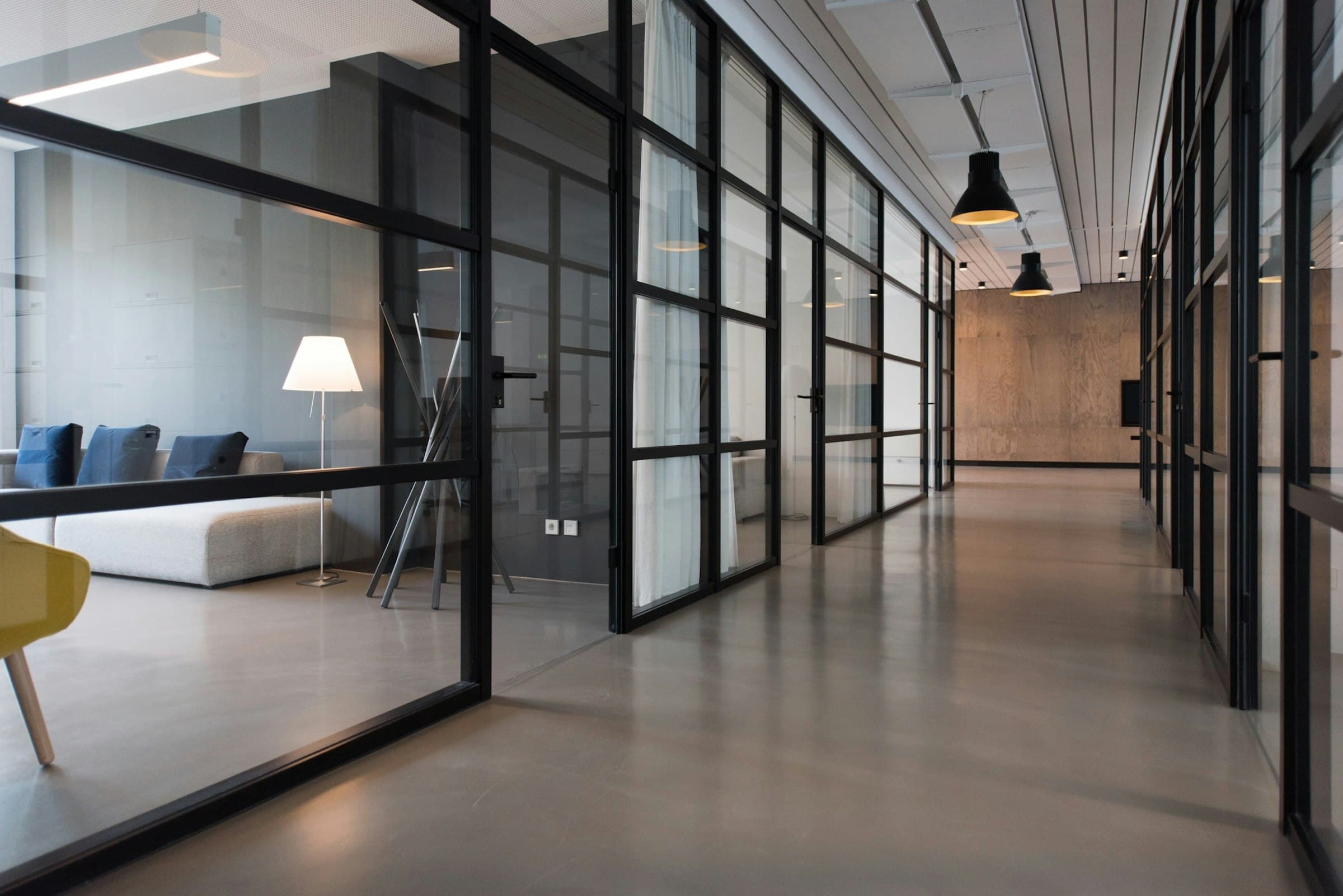 An empty modern office corridor with black-framed glass partitions and daylight.