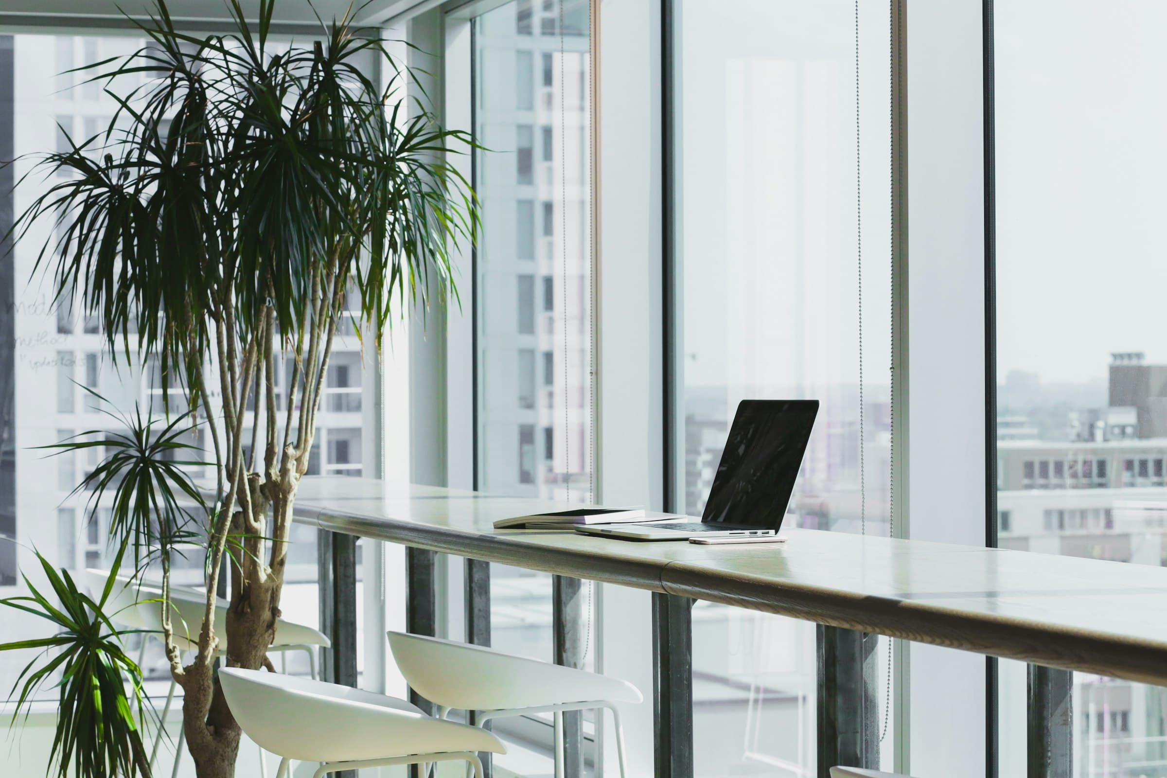 A high-rise office interior with a laptop on a glass desk and a city skyline through floor-to-ceiling windows.